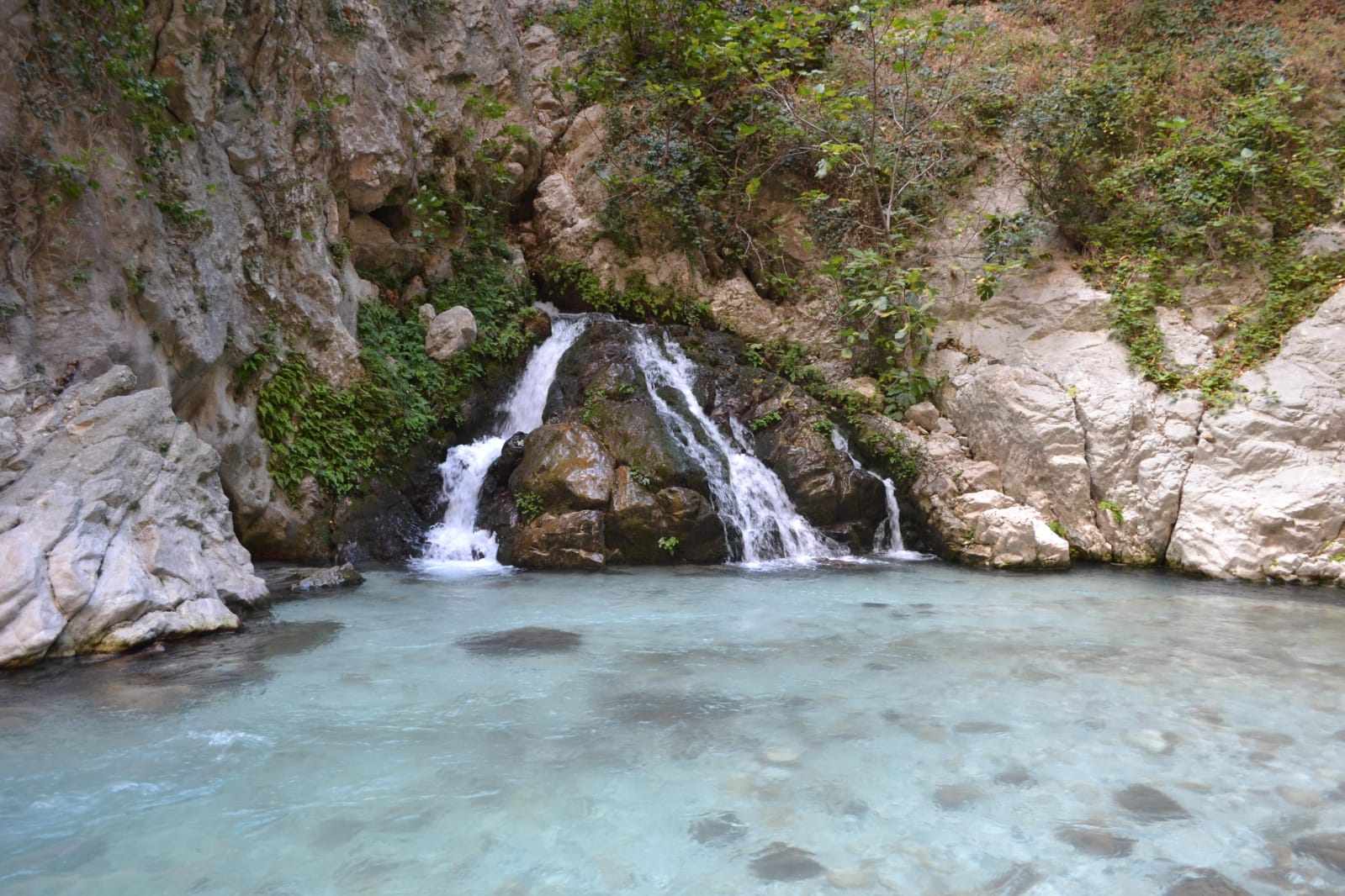 Sunlight filtering into a narrow section of Saklıkent Gorge, illuminating the pale limestone walls above the stream